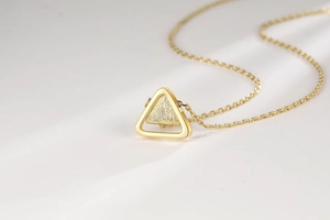 Macro shot of gold triangle necklace featuring brushed metal texture and hollow frame