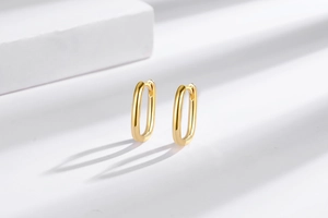 Detailed view of polished 18K gold plated oval huggie earrings with a sleek mirror finish