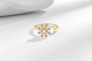 Detail of a rotating daisy flower ring with pink and blue stones on white rock
