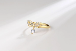 Detail view of gold bow ring featuring micro-pave diamonds and hanging zircon stone
