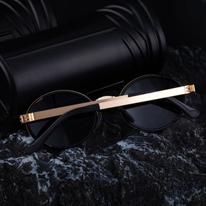 Close-up of polarized oval sunglasses with gold metal hinges on a dark stone base