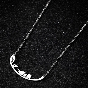 Détail du pendentif branche avec silhouettes d'oiseaux et feuilles en métal argenté