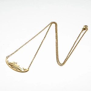 Détail macro d'un collier en acier doré avec un pendentif évidé aux motifs de vague et d'oiseau