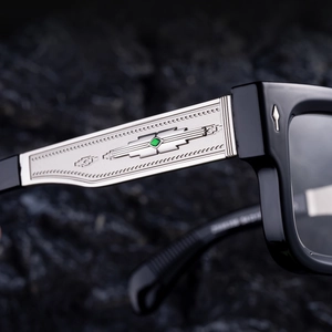 Vue macro des lunettes noires carrées avec charnières gravées argent et pierre verte