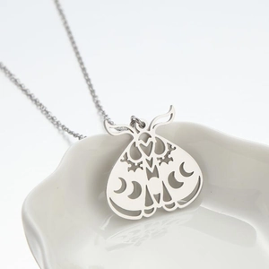 Macro shot of silver moth pendant with hollow crescent moon and floral cutout details