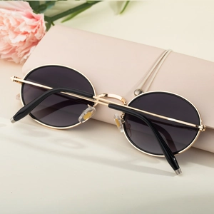 Détail de lunettes de soleil ovales en métal avec verres noirs sur un sac en cuir rose