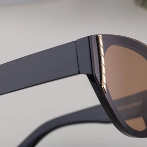 Detailed macro view of shiny black cat-eye frame with gold metal stripe accents