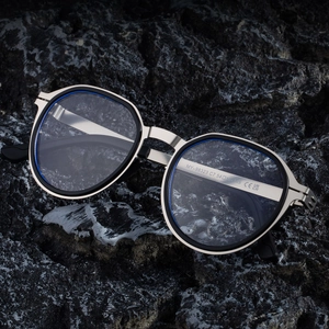 Modern geometric silver metal sunglasses with blue trim on black rock surface