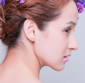 Close-up of golden double heart stud earrings worn by a model with floral accents