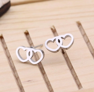 Detail view of silver heart-shaped stainless steel earrings on a wooden display stand