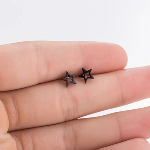 Close-up of minimalist matte black star studs held on finger to show compact scale
