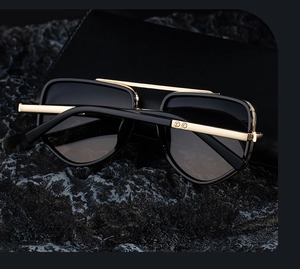 Gros plan de lunettes de soleil carrées noir et or avec pont en métal sur roche