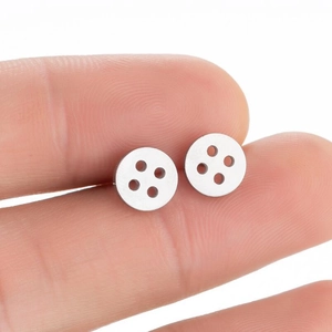 Detailed close-up of small silver button earrings in polished stainless steel held by hand