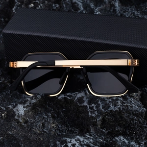 Detail of square polarized sunglasses with black frame and golden metal edges on stone