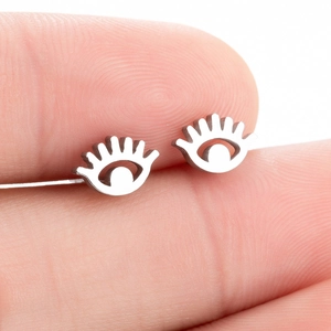 Macro shot of silver devil eye stud earrings held on fingertips showing small scale