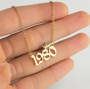 Close-up of gold stainless steel necklace with crown 1980 year pendant for women