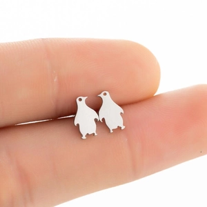 Minimalist cute penguin stud earrings in matte silver finish shown on a finger for scale