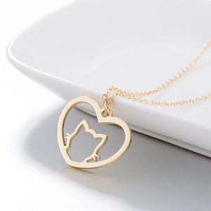 Collier chat en acier doré avec pendentif cœur évidé posé sur une assiette en céramique