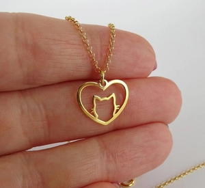 Détail d'un collier doré avec pendentif silhouette de chat dans un cœur évidé