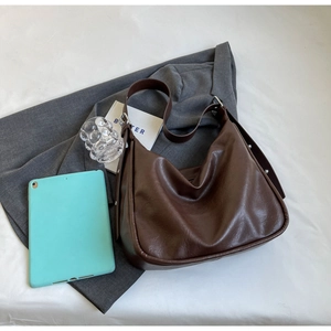 Detail of dark brown leather hobo bag with adjustable buckle strap and laptop on suit