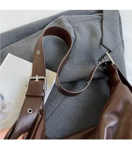 Detail of adjustable brown leather shoulder strap with silver metal buckle on bucket bag