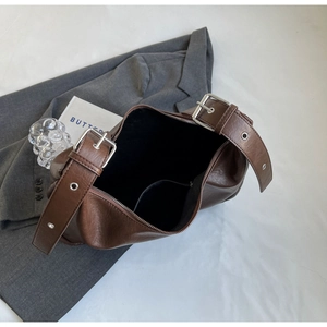 Detail view of large brown bucket bag with wide strap and silver metal buckle closure