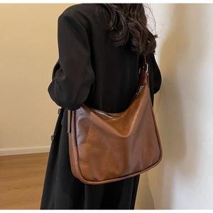 Detailed view of brown retro hobo bag worn by a model in a minimalist indoor setting