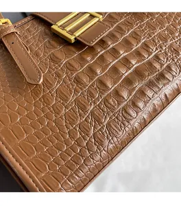 Close-up of brown crocodile embossed leather handbag with premium gold metal buckle detail