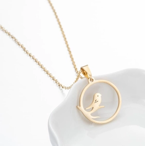 Detailed view of a gold-plated stainless steel bird charm necklace in a white ceramic dish