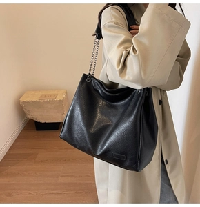 Dettaglio della grande borsa tote nera con tracolla a catena e targa indossata su trench beige