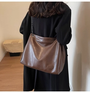 Dettaglio della borsa a tracolla in ecopelle marrone con catena in metallo su modella