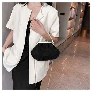 Detail of black lace evening clutch bag featuring pearl handle and gold chain strap