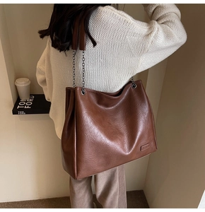 Dettaglio della borsa tote in pelle marrone con tracolla a catena indossata da modella
