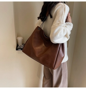 Dettaglio della borsa tote in pelle litchi marrone caramello con catena e logo alla moda
