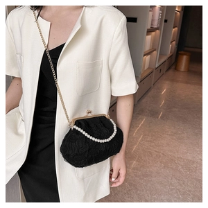 Black lace crossbody bag with pearl handle and metal clasp shown on a model