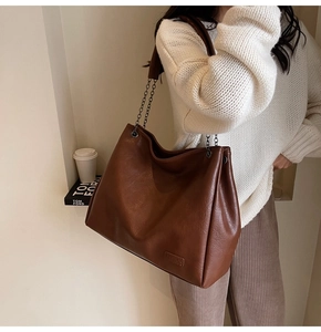 Dettaglio di una borsa tote marrone con tracolla a catena e targhetta 'FASHION'