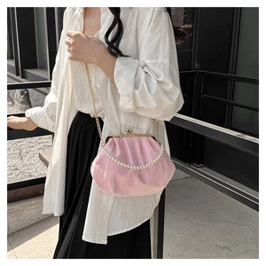 Pink pleated cloud bag with pearl strap and gold chain shown in a stylish lifestyle setting