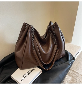 Dettaglio borsa tote in pelle marrone scuro con tracolla a catena e logo in metallo