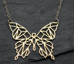 Macro view of golden hollow geometric butterfly pendant on a dark stone background