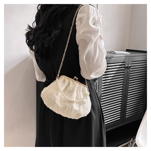 Detail of white pleated cloud bag with pearl handle and gold chain worn by a model