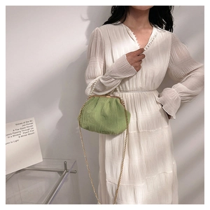 Detail of green ruched bag with pearl handle and metal chain on a white dress