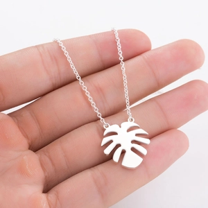 Close-up of a silver monstera leaf pendant necklace held in hand with fine chain details