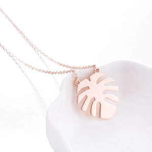 Rose gold stainless steel monstera leaf pendant necklace on white ceramic surface