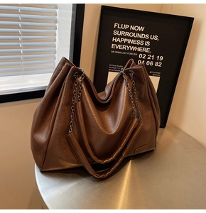Dettaglio di una borsa tote marrone su tavolo in metallo con pelle lucida e tracolla a catena