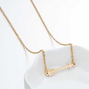 Detailed close-up of a gold arrow pendant necklace on a white ceramic display