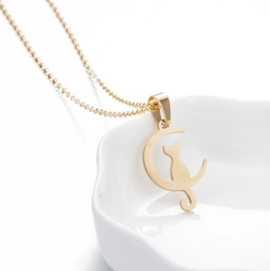 Close-up of a minimalist gold cat sitting on a crescent moon pendant in a white dish