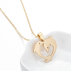 Detail of gold-plated dolphin heart pendant necklace on a minimalist ceramic tray