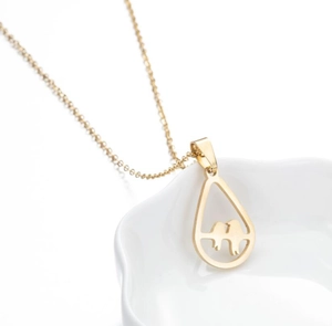Close-up of a gold teardrop pendant with bird motif on a textured white surface