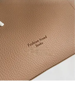 Macro detail of dark khaki litchi grain leather tote bag with debossed logo texture