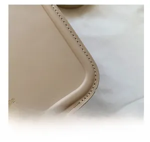 Macro shot of precise stitching and gold embossed logo on a beige leather handbag